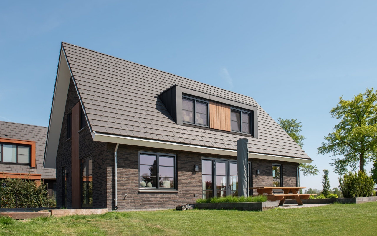 Vrijstaande villa opgetrokken met donkere baksteen en lichte houtaccenten.