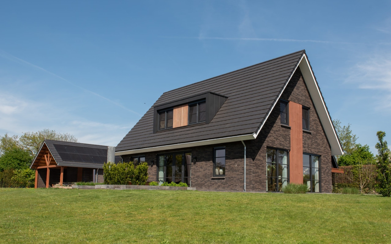Vrijstaande villa opgetrokken met donkere baksteen en lichte houtaccenten.