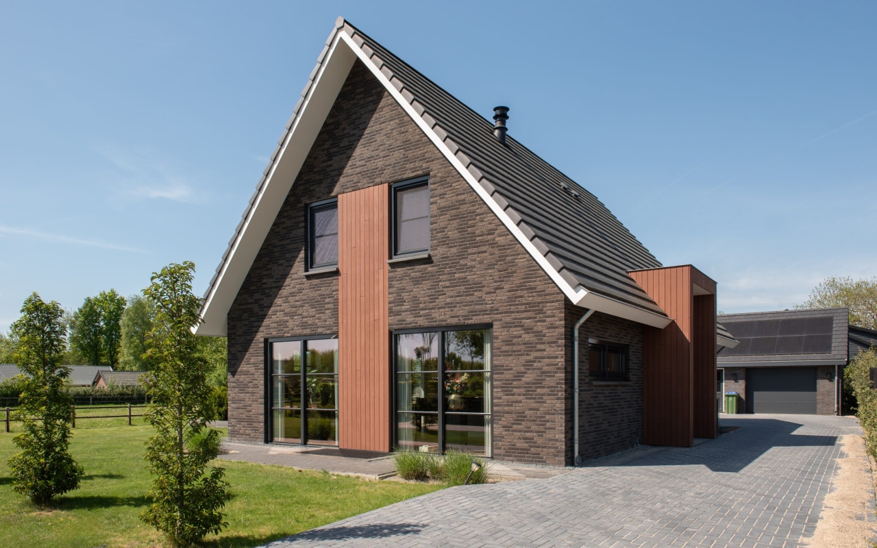 Vrijstaande villa opgetrokken met donkere baksteen en lichte houtaccenten.