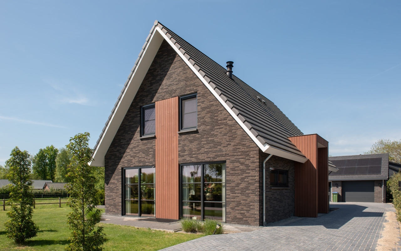 Vrijstaande villa opgetrokken met donkere baksteen en lichte houtaccenten.
