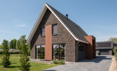 Vrijstaande villa opgetrokken met donkere baksteen en lichte houtaccenten.